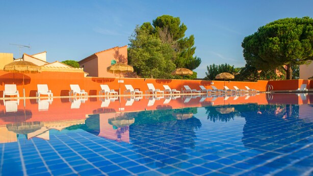Ein Pool mit Liegestühlen und Sonnenschirmen, umgeben von Bäumen und Gebäuden.