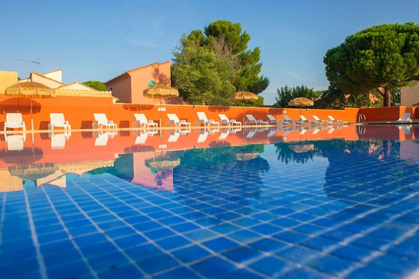 A swimming pool with lounge chairs and umbrellas, surrounded by trees and buildings.