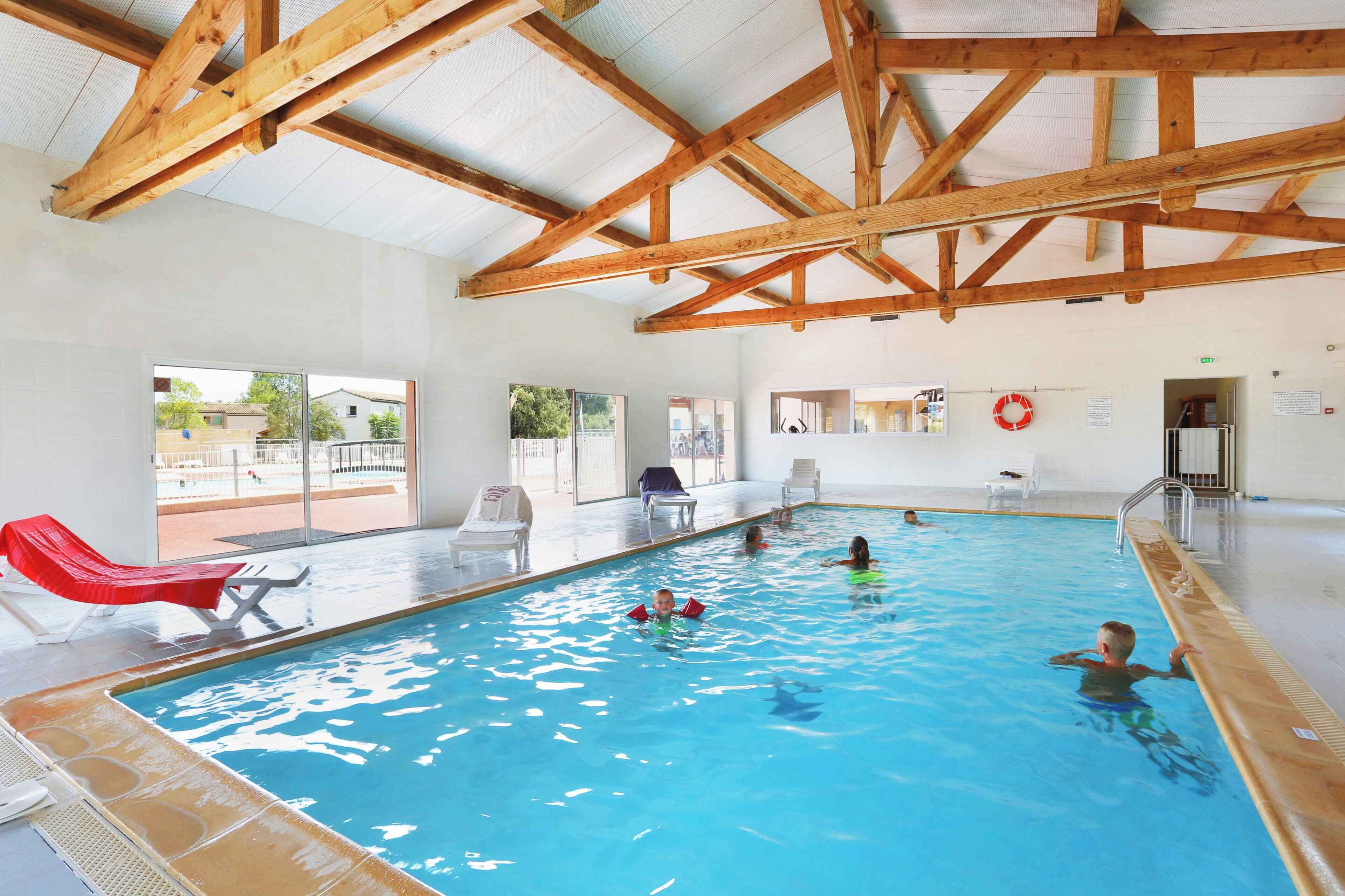 An indoor swimming pool with wooden beams, clear glass walls, and a lifebuoy.