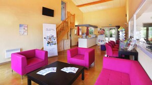 A lobby with bright pink seating, a staircase, a reception desk, and informational posters. - Charmant T3 au cœur d’un domaine de 6 ha | Piscine (Sauve)
