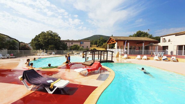 A swimming pool with lounge chairs, a shaded area, and a building with a tiled roof. - Charmant T3 au cœur d’un domaine de 6 ha | Piscine (Sauve)