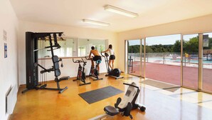A gym with exercise equipment, large windows, and a view of an outdoor area. - Charmant T3 au cœur d’un domaine de 6 ha | Piscine (Sauve)
