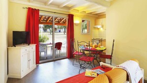A room with a bed, a TV on a cabinet, a dining table with chairs, and a sliding glass door leading to an outdoor area. - Mas Cévenols au cœur d’un domaine | Accès piscines (Sauve)