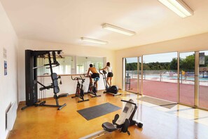 Un gimnasio con equipo de ejercicio, ventanas amplias y vistas a un espacio exterior.