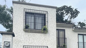 A two-story building with a white exterior, multiple windows with black railings, and potted plants on the balconies.