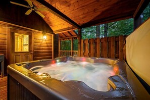 A hot tub in a wooden cabin with a ceiling fan and a view of trees. - Silver Spur (Broken Bow)