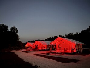 A row of red-roofed tents with string lights, arranged in a campsite.