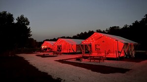 A row of red-roofed tents with string lights, arranged in a campsite. - Deluxe Safari Tent with Fire Pit, Hammocks & BBQ in Basinger, Florida (Okeechobee)