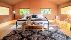 A cozy room with a bed, a small table, two chairs, and a window with a view of greenery. - Deluxe Safari Tent with Fire Pit, Hammocks & BBQ in Basinger, Florida (Okeechobee)