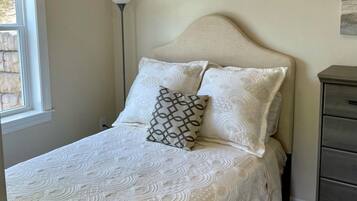 A bedroom with a bed, a bedside lamp, a dresser, and a window.