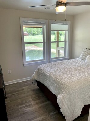 A bedroom with a bed, two windows, a ceiling fan, and a view of a green landscape. - Incredible Waterfront Cabin for a Peaceful Family Getaway near Purlear, North Carolina (Purlear)