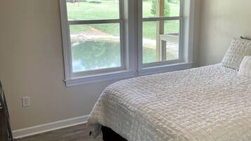 A bedroom with a bed, two windows, a ceiling fan, and a view of a green landscape.