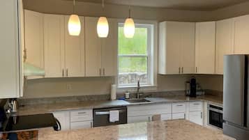 A modern kitchen with white cabinets, a granite countertop, a stainless steel refrigerator, and pendant lighting.