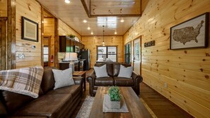 A cabin interior with wooden walls, a living room with two leather sofas, a coffee table, and a kitchen area. - Mountain Retreat with Perfect for Groups in Pigeon Forge, Tennesee (Pigeon Forge)