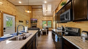 A wooden cabin interior with a kitchen featuring granite countertops, a built-in microwave, and a stone fireplace. - Mountain Retreat with Perfect for Groups in Pigeon Forge, Tennesee (Pigeon Forge)