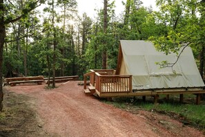 Un camping con una tienda de campaña, una terraza de madera y mesas de picnic.