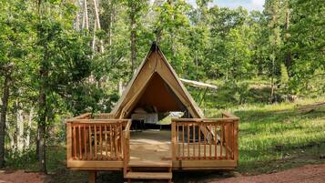 A triangular wooden cabin with a deck and a bed inside.