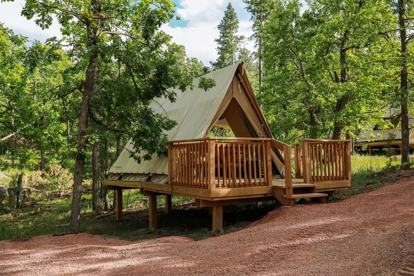 A wooden deck with a tent structure, surrounded by trees.