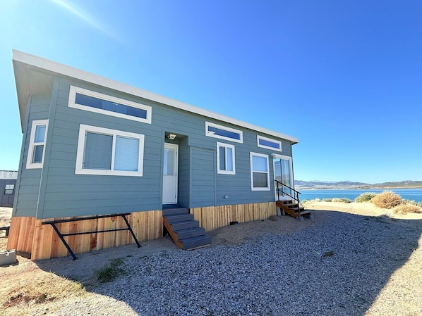 A single-story, light blue building with a front door, a small porch, and a set of stairs leading to a deck.