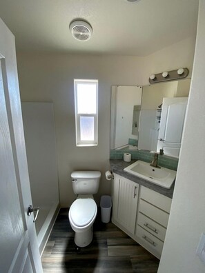 Une petite salle de bain comprenant des toilettes, un lavabo et un meuble-vasque, avec une fenêtre et une bouche d’aération au plafond.