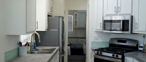 A compact kitchen with white cabinets, a stainless steel refrigerator, a microwave, and a gas stove.