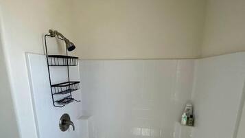 A white shower stall with a metal showerhead, a black towel rack, and a small bottle on the wall.