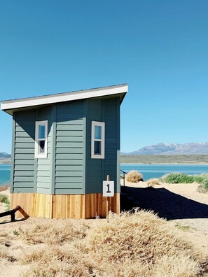 A small, single-story building with a wooden deck, a number '1' sign, and a view of a lake and mountains.