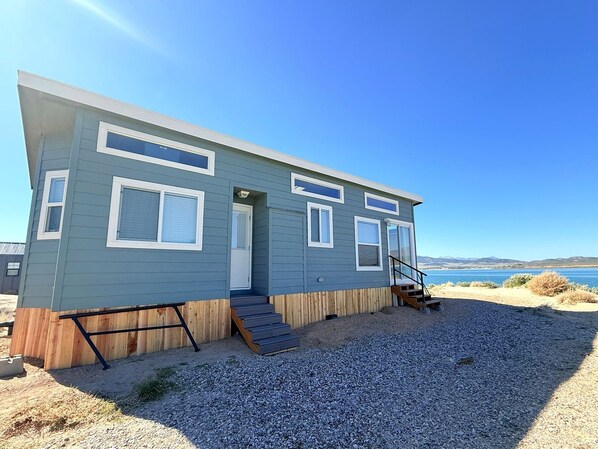 A single-story, light blue building with a front door, a small porch, and a set of stairs leading to a deck.