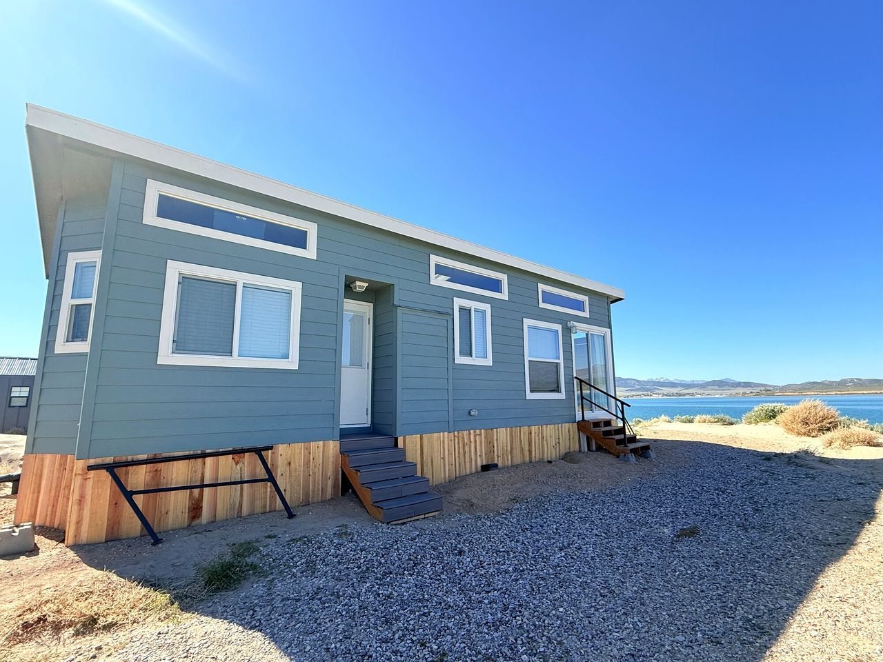 A single-story, light blue building with a front door, a small porch, and a set of stairs leading to a deck.