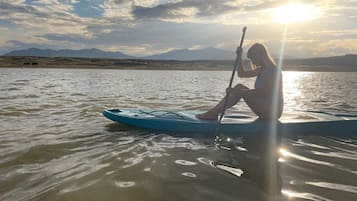 Eine Person steht auf einem Paddleboard auf ruhigem Wasser, mit blauem Himmel und Bergen im Hintergrund.