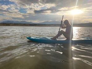 Una persona haciendo paddleboard sobre aguas tranquilas, con cielo despejado y montañas a lo lejos.