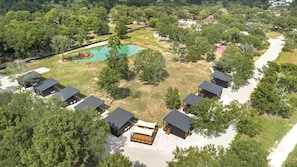 Vue aérienne d’un complexe hôtelier comprenant plusieurs chalets, une piscine et une végétation luxuriante.