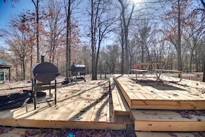 A wooden deck with barbecue grills and a picnic table in a wooded area.