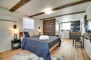 Ein Schlafzimmer mit Bett, Nachttischen, Schreibtisch, Stuhl, Fenster und einer Küchenzeile.