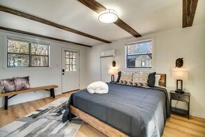 Ein Schlafzimmer mit einem großen Bett, Holzbalken, einer Bank, zwei Nachttischen mit Lampen und Blick durch ein Fenster.