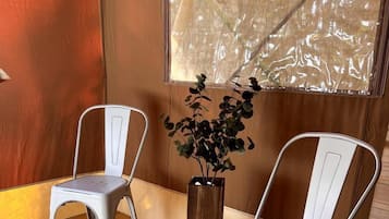 Two white metal chairs, a wooden floor, a window with a view, and a potted plant.