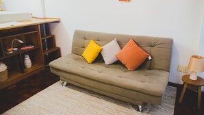 A living room with a sofa, a wooden side table, a lamp, and a bookshelf. - Apto Climatizado com Wi-fi no Centro de Bel m (Belém)