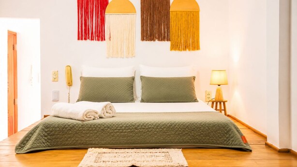 A bed with a green quilt, two pillows, a white duvet, a rolled white towel, a wooden bedside table with a lamp, and a wall-mounted telephone. - Apto Climatizado com Wi-fi no Centro de Bel m (Belém)