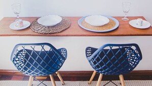 A dining area with a wooden table, two blue chairs, and woven placemats. - Apto Climatizado com Wi-fi no Centro de Bel m (Belém)