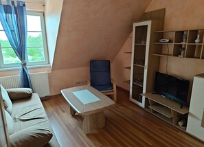 A cozy room with a sofa, a small table, a TV, and a cabinet with shelves.