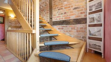 A wooden staircase with blue carpeted steps and a brick wall.