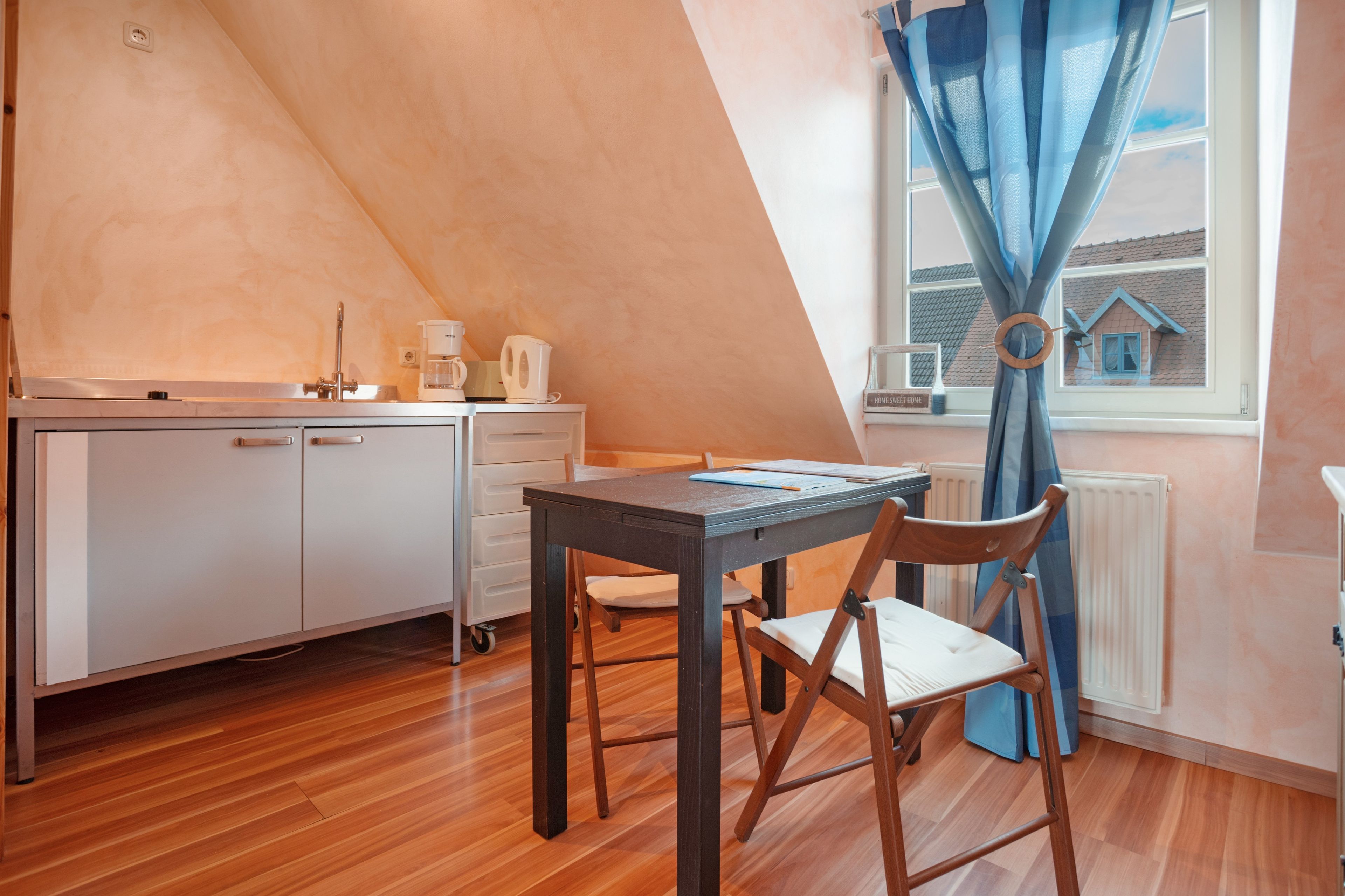 A small, cozy kitchen with a wooden table and chairs, a white cabinet, and a window with curtains.