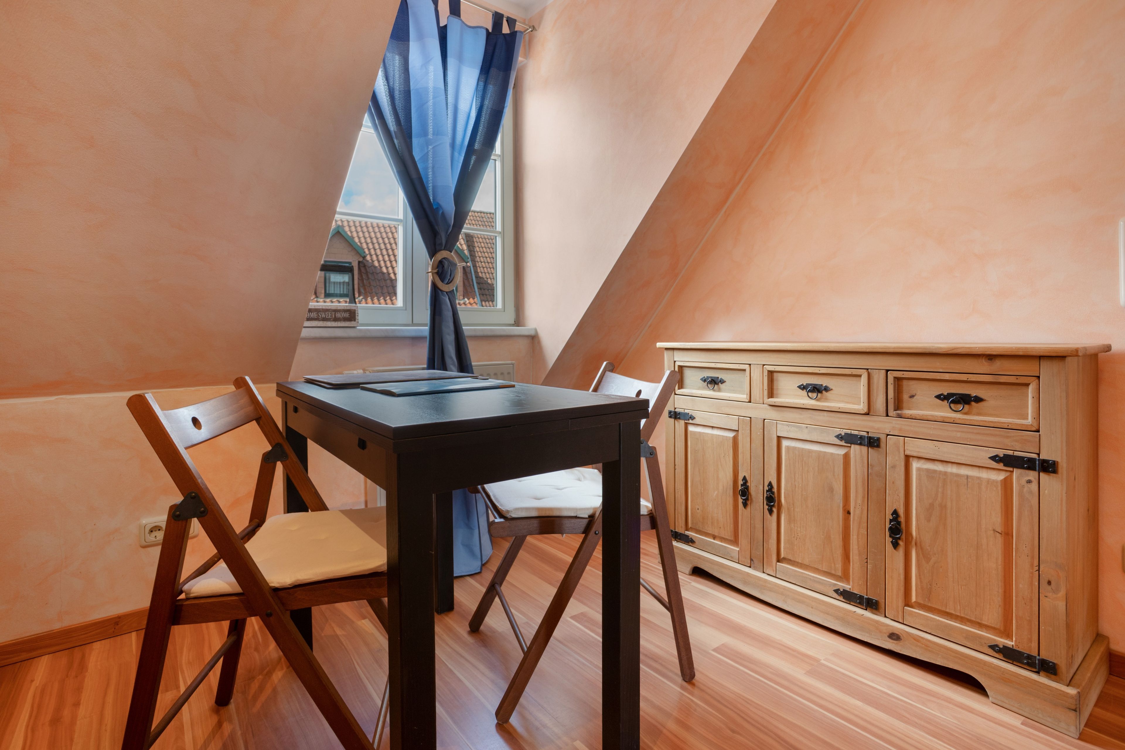 A dining area with a table and chairs, a window with curtains, and a wooden cabinet.