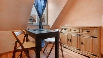 A dining area with a table and chairs, a window with curtains, and a wooden cabinet.