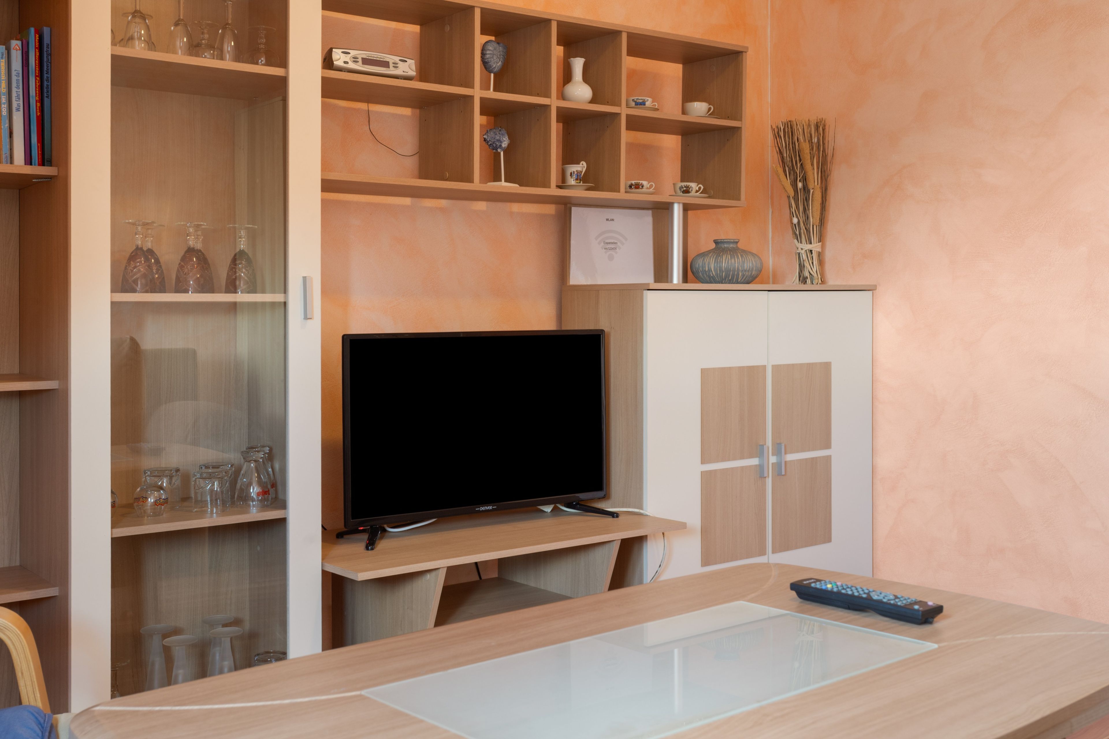 Ein modernes Wohnzimmer mit Flachbildfernseher, Holzregalen mit Dekoration und einem Couchtisch mit Glasplatte.