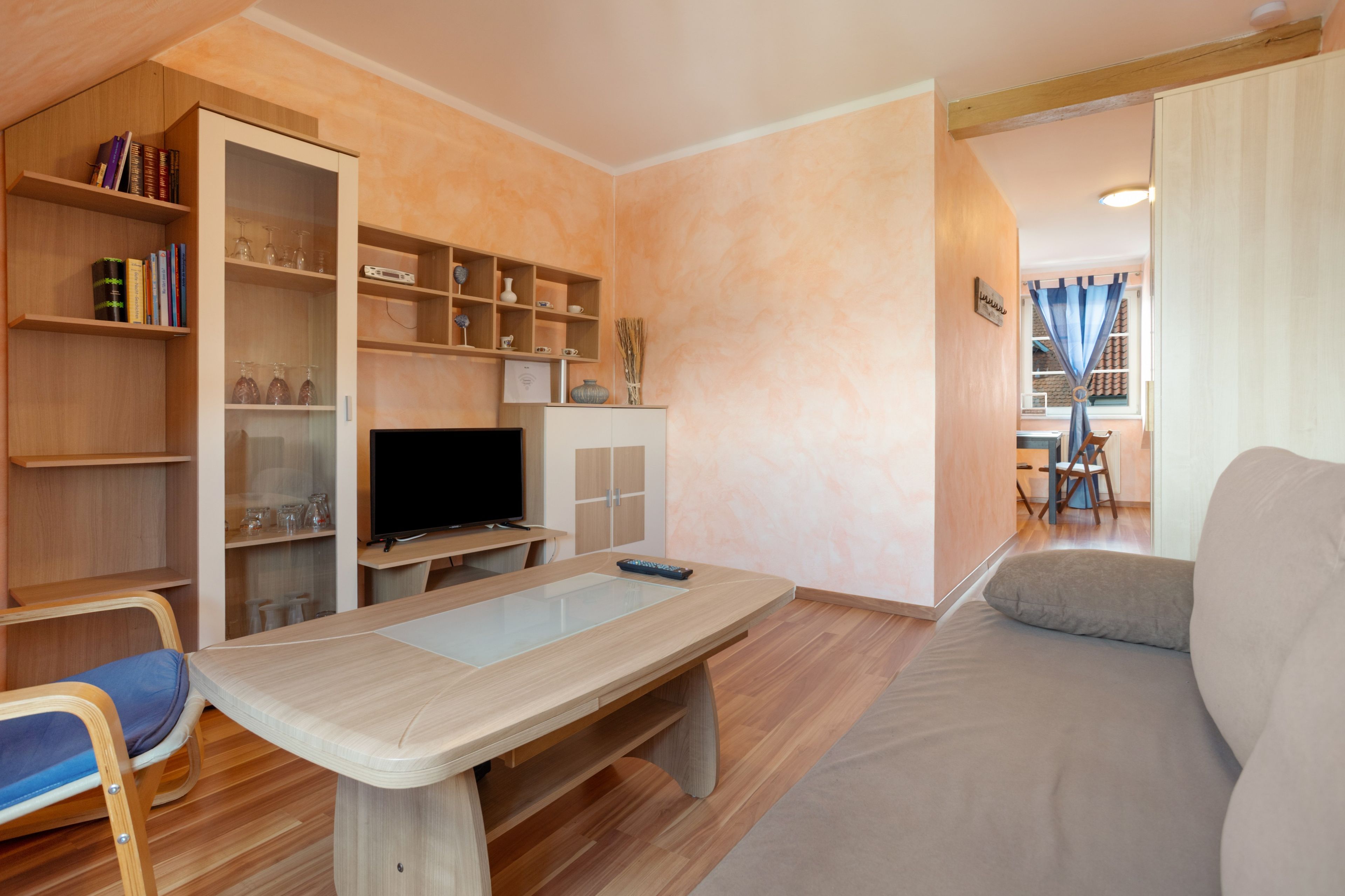 A living room with a sofa, a TV, a wooden table, and built-in shelving with books and decorative items.