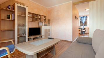 A living room with a sofa, a TV, a wooden table, and built-in shelving with books and decorative items.