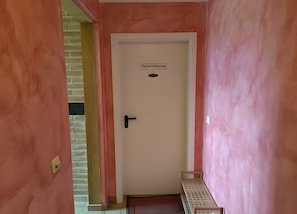 Ein Flur mit einer Tür, auf der 'Ferienwohnung' steht, einer Bank und einer Backsteinwand.