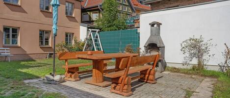 Un patio con una mesa y bancos de madera, un muro de ladrillo y una chimenea.