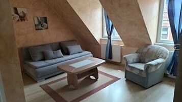Un salon moderne comprenant un canapé, un fauteuil et une table basse, avec un plafond en pente et de grandes fenêtres dotées de rideaux.